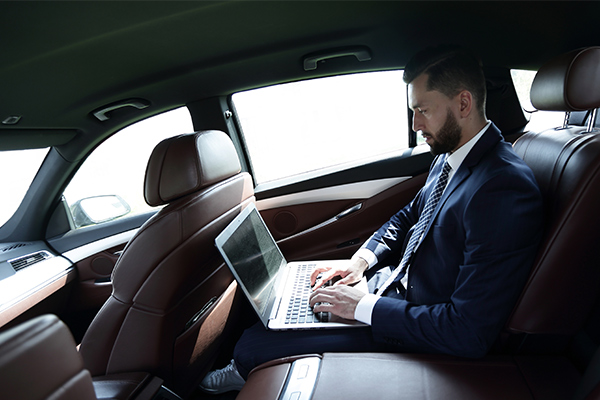 Social-Media-Investigation-Services-V2 business man in the back of a car typing on a laptop